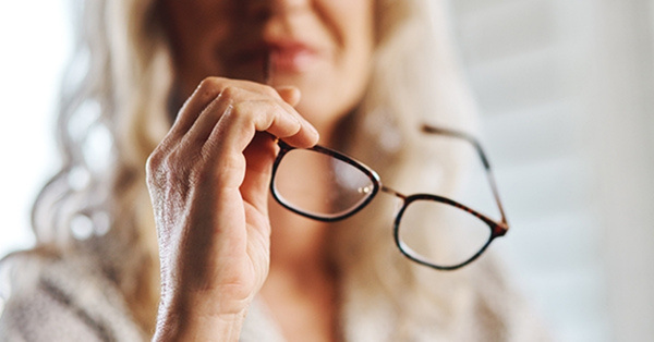 Businesswoman holding eyeglasses, blurred background focus on glasses.