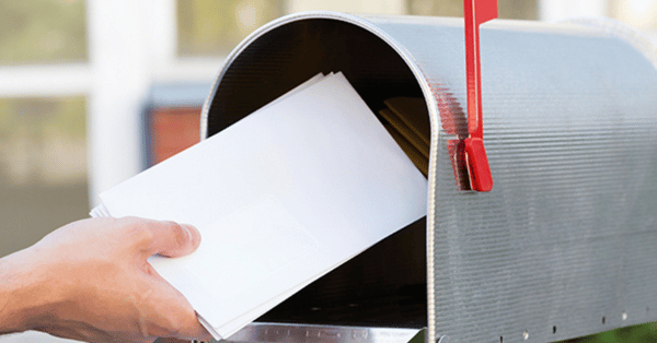 Hand inserting letters into a metal mailbox outdoors.