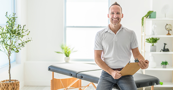 A smiling chiropractor holding pad in hospital and looking at camera