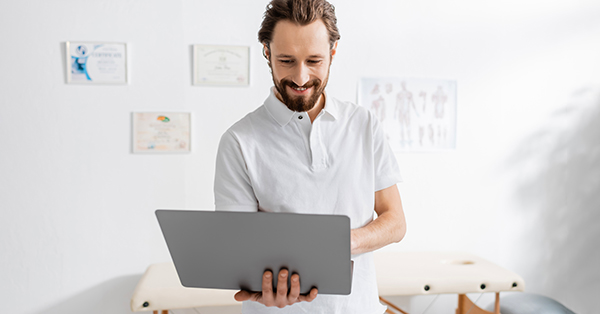 smiling chiropractor using laptop to enhance patient engagement