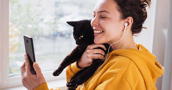 cheerful young woman wearing headphones-holding smartphone and a cat