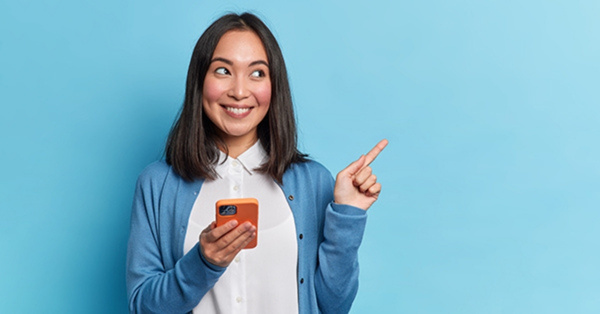 Smiling Asian woman holding smartphone pointing sideways