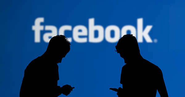 Silhouette of two people using phones with Facebook logo backgroun