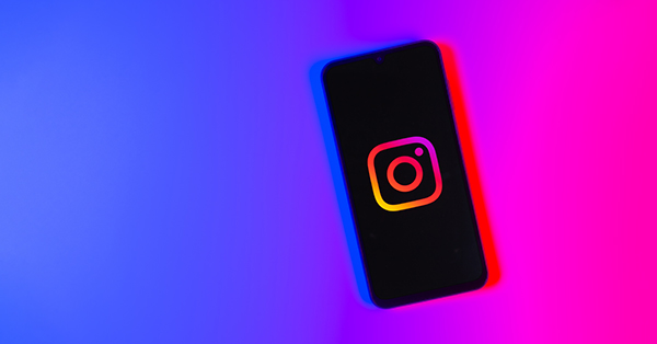 Smartphone with glowing Instagram logo on purple pink background.