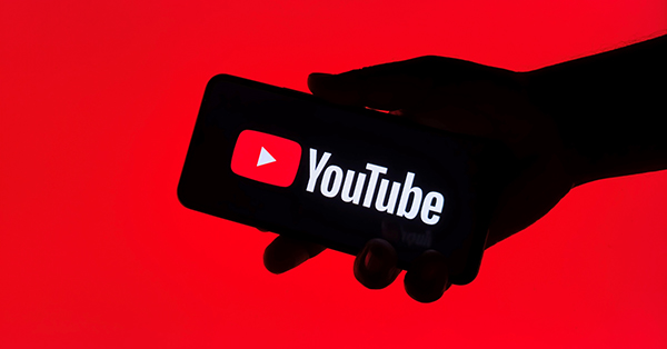 Hand holding smartphone showing YouTube logo on red screen.