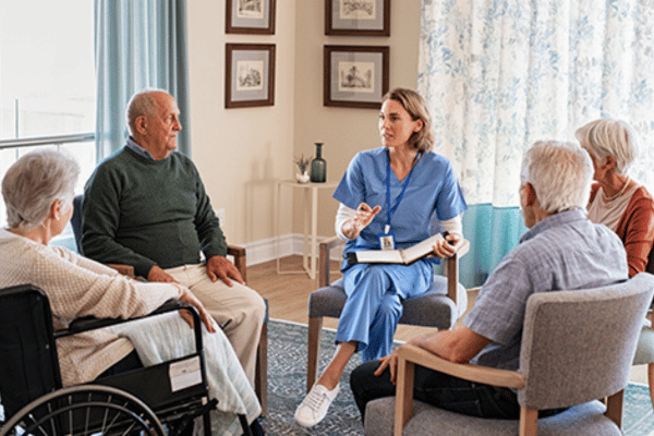 A healthcare professional leads an educational discussion with a small group of older adults in a clinic setting.