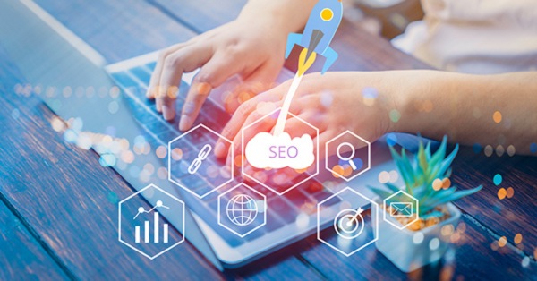 Hands typing on laptop with SEO and digital icons.