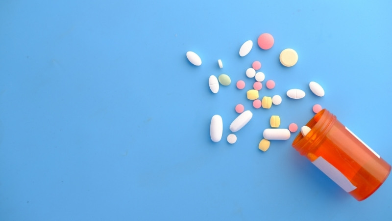Spilled orange pill bottle with assorted colorful tablets on blue.